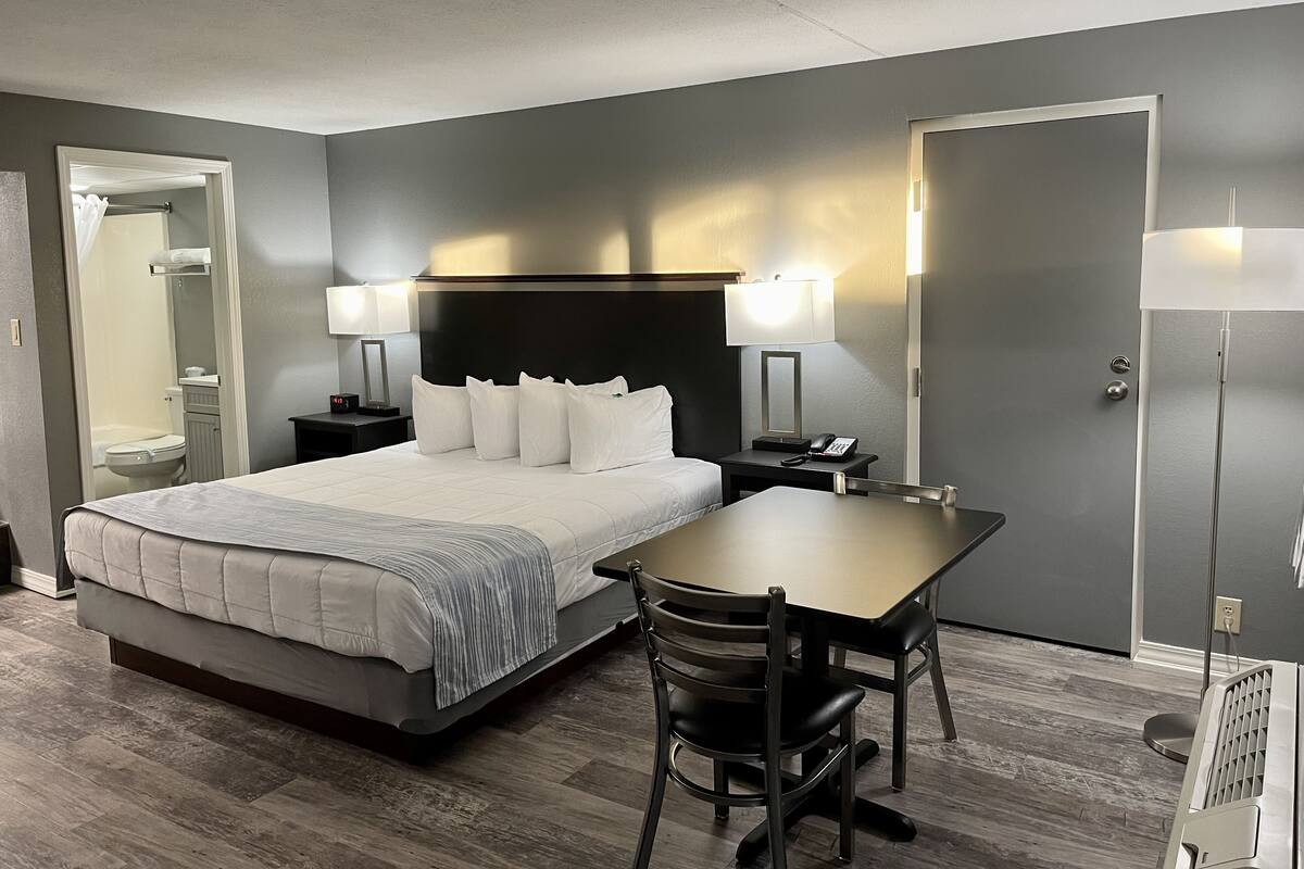 A hotel room with a bed, bedside tables, a desk, chairs, and a mirror.