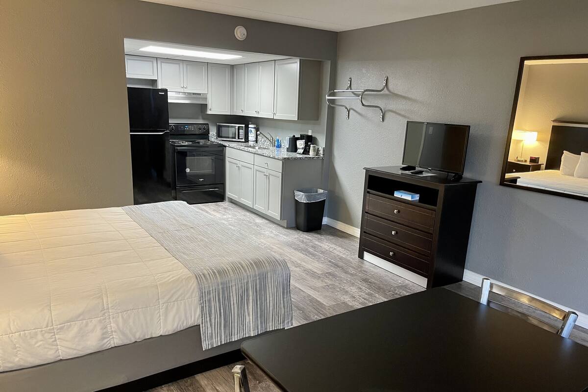 A hotel room with a bed, a desk, a TV, a small kitchenette, and a bathroom.