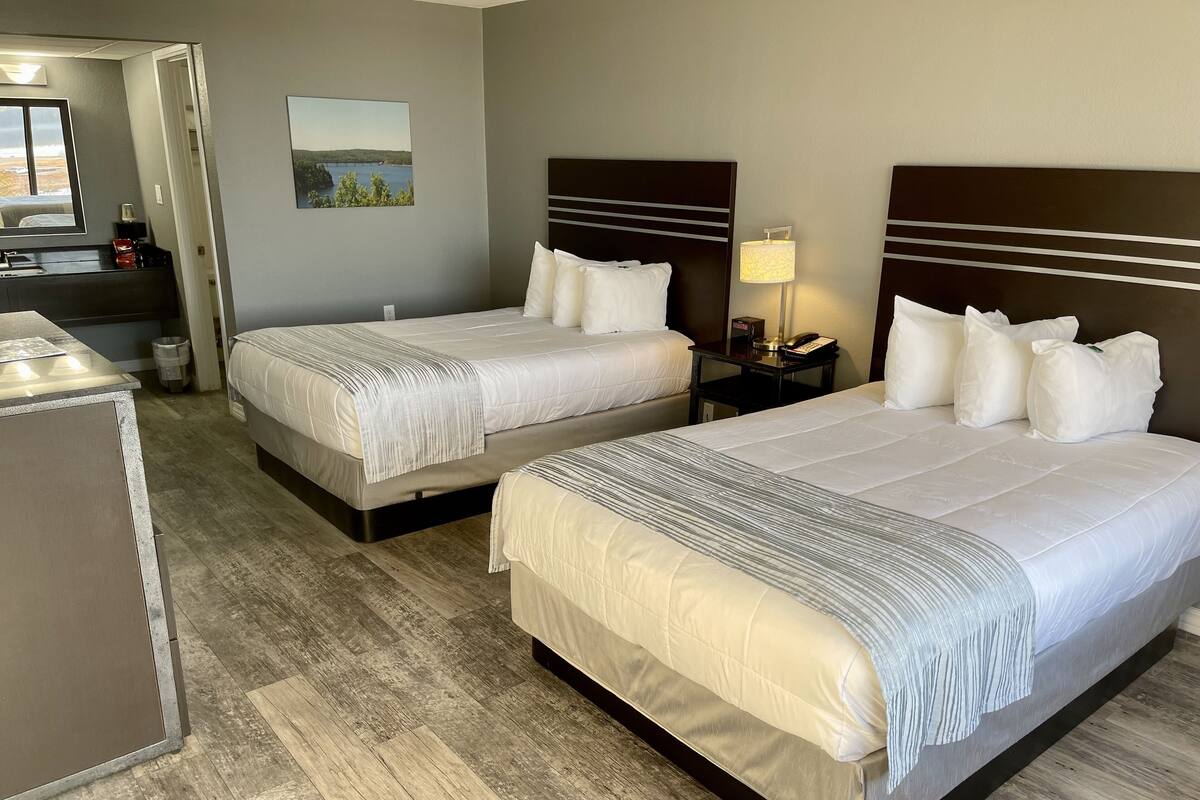 A hotel room with two beds, a desk, and a nightstand with a lamp.