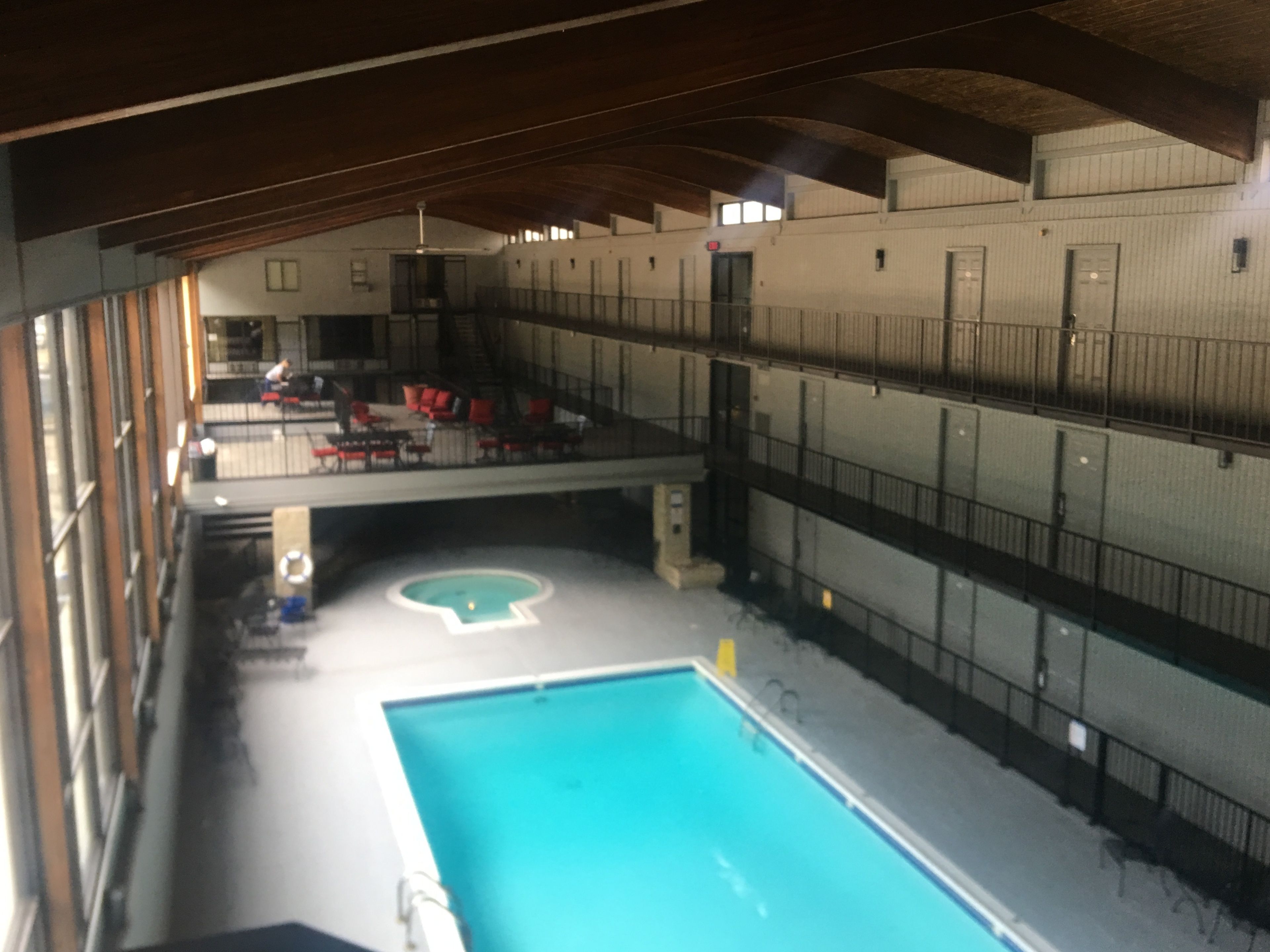 Une piscine intérieure dotée d’un plongeoir, entourée d’un haut plafond et de rampes métalliques.