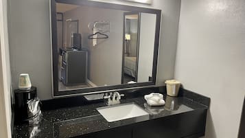 A bathroom with a black countertop, a white sink, a mirror, and a towel dispenser.