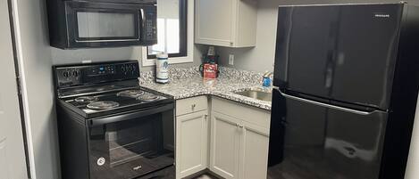 A kitchen with a black stove, microwave, and refrigerator, light gray cabinets, and a granite countertop.