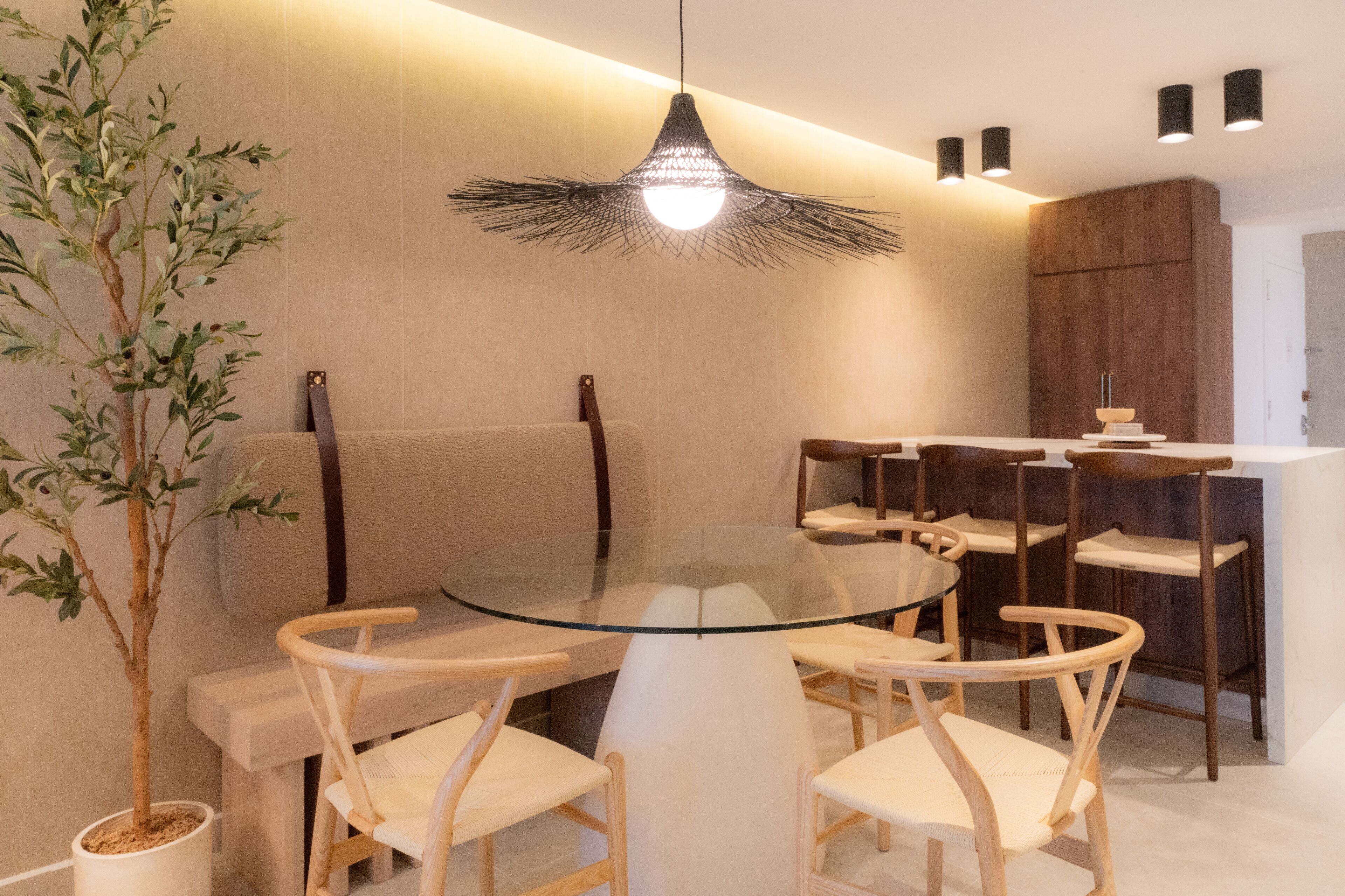 A modern dining area with a glass table surrounded by wooden chairs, a hanging light fixture, and a potted plant.