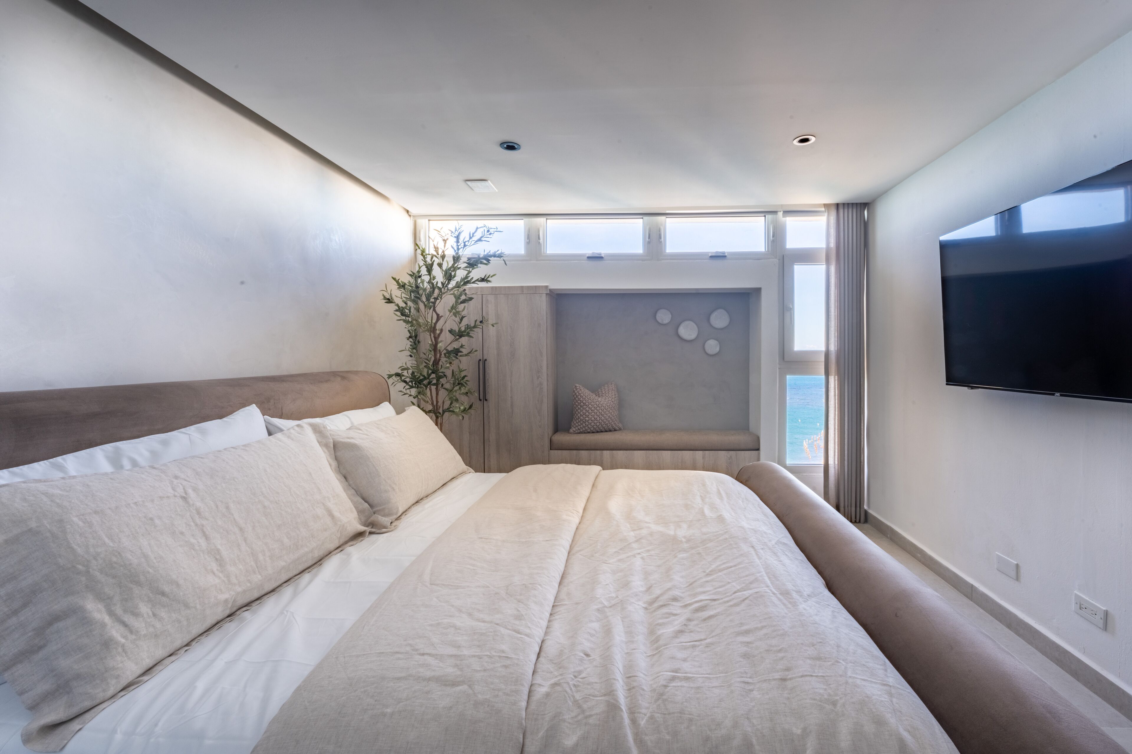 Ein modernes Schlafzimmer mit einem großen Bett, einer Sitzecke mit Aussicht und einem an der Wand montierten Flachbildfernseher.