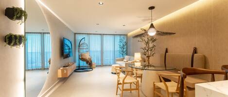 A modern living room with a glass dining table, wooden chairs, a sofa, and a hanging plant.