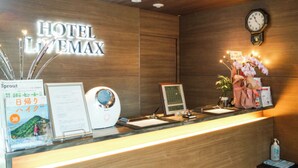 Un mostrador de recepción de hotel con detalles de madera, un reloj, una pantalla digital y un arreglo floral.
