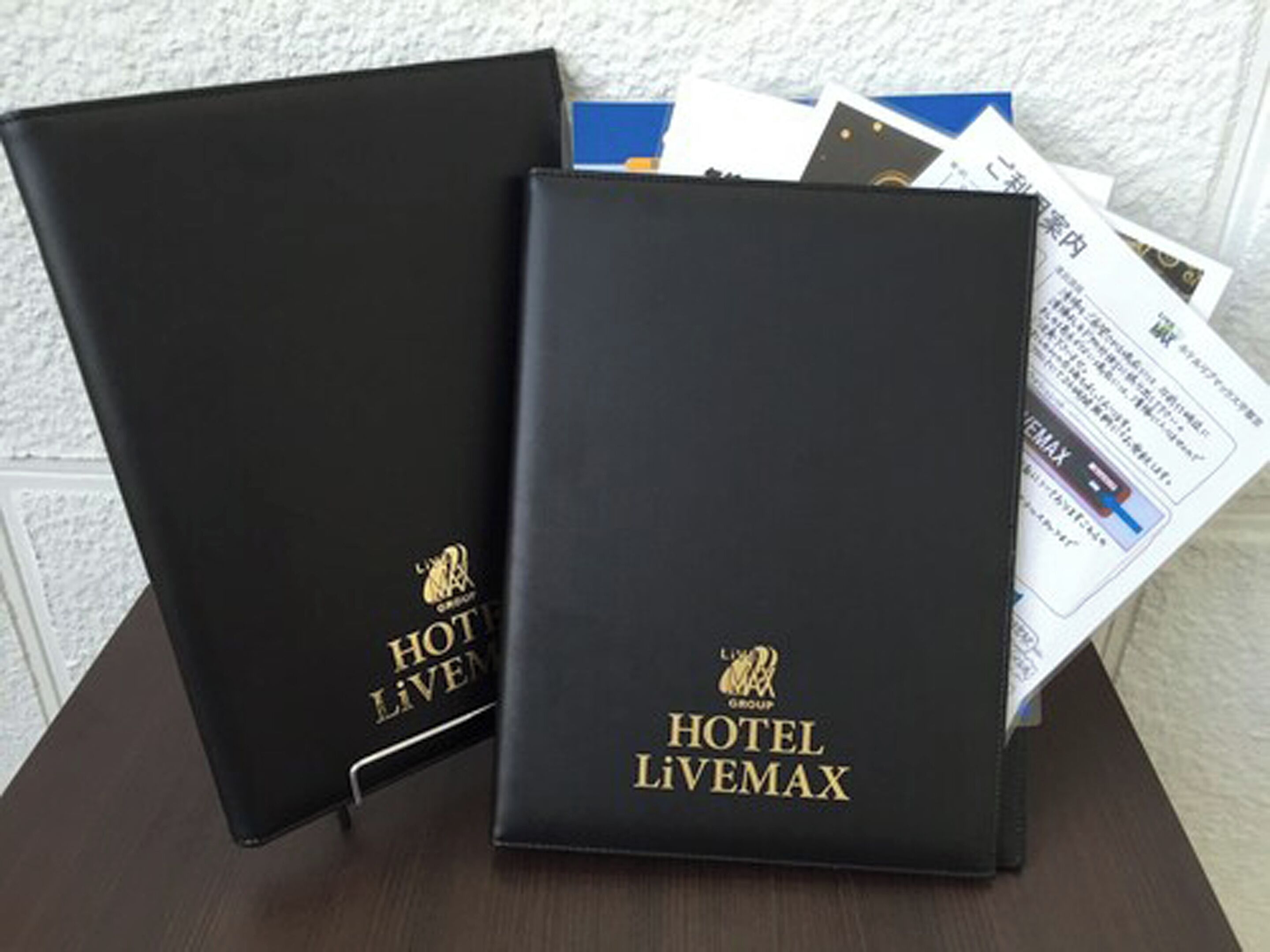 Deux classeurs noirs portant la marque « HOTEL LIVEMAX » et un logo, placés sur une table avec quelques documents.