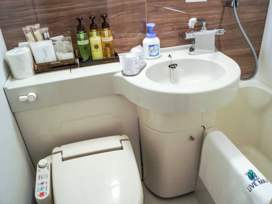 A bathroom with a toilet, a sink, and a shower. There are toiletries on the sink counter.