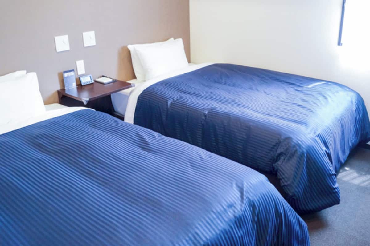 A hotel room with two beds, a nightstand, a desk, and a window.