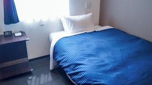 Habitación de hotel con una cama individual, una mesita de noche, un escritorio y una ventana con cortinas.
