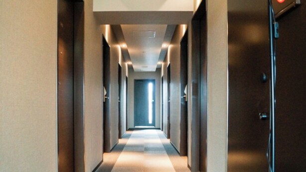 Un pasillo de hotel con piso a cuadros, puertas a ambos lados y una luz al final.