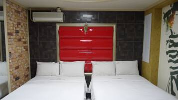 A hotel room with two beds, a red headboard, and a brick wall.