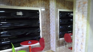 A corner of a room with a red table and chairs, a green chair, and a mirror reflecting a black object. - Songdo Blue Hotel (Incheon)