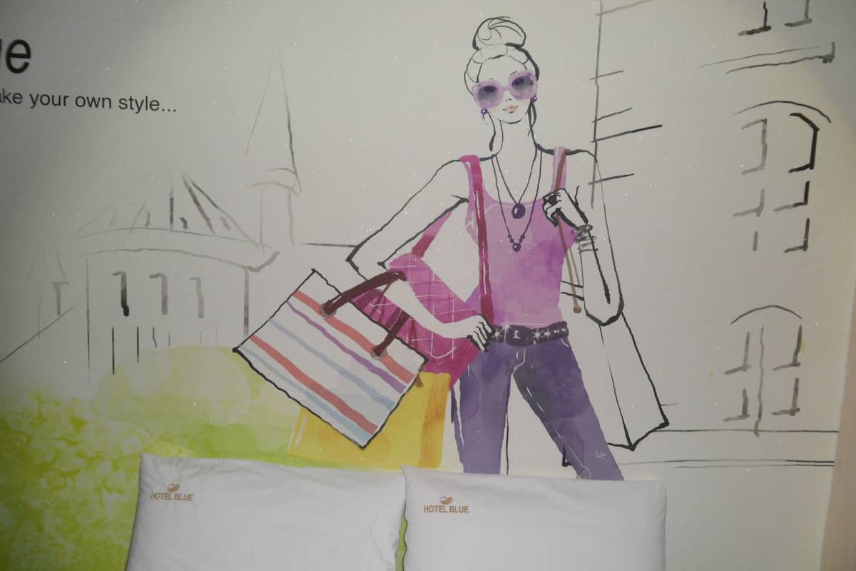 A sketch of a person with shopping bags, a necklace, and sunglasses, with a building in the background.