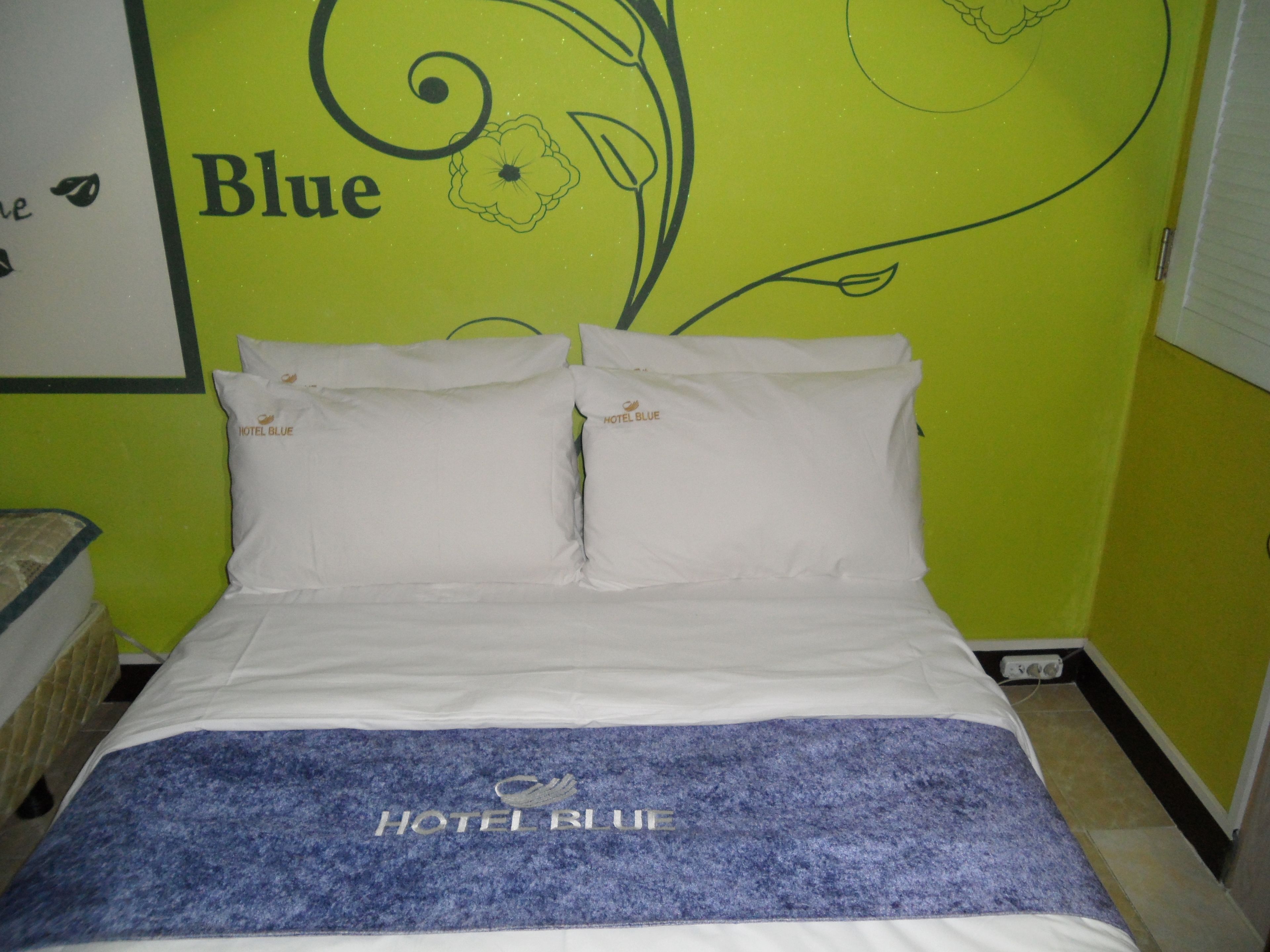 A hotel room with a bed, pillows, and a wall with a floral design and the word "Blue".