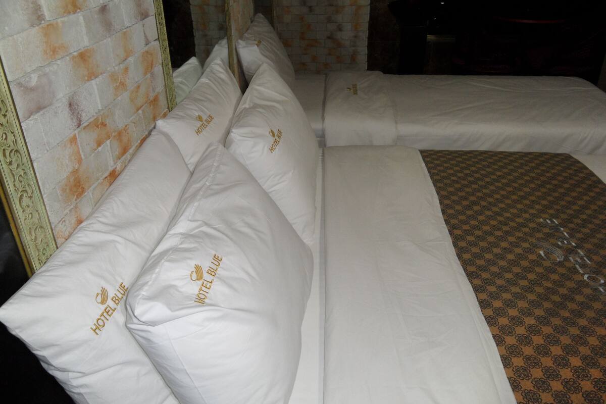 A hotel room with a large bed, white bedding, and pillows labeled 'Hotel Blue'.