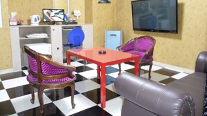 A room with a checkered floor, a television mounted on the wall, a desk with a chair, and two armchairs with purple cushions. - Songdo Blue Hotel (Incheon)