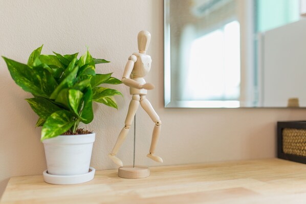 Un maniquí de madera sobre un soporte, junto a una planta en maceta, todo sobre una superficie de madera.