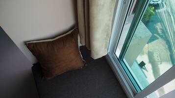 Canto de um quarto com carpete cinza escuro, travesseiro marrom e janela com vista para uma rua e carros estacionados.