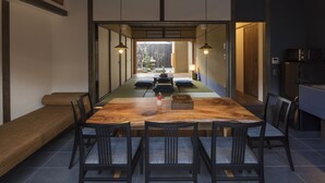 A traditional Japanese-style dining room with a long wooden table, black chairs, and a view of a garden through a sliding door. - Sanjusangendo Yoitsubaki (Kyoto)