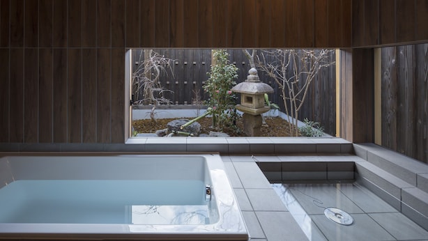 A modern bathroom with a large bathtub, a window with a view of a garden, and a wooden wall. - Sanjusangendo Yoitsubaki (Kyoto)