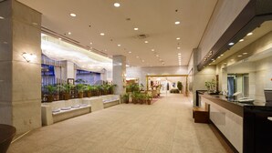 Een ruime lobby met een marmeren vloer, een receptiebalie en een zithoek met planten.