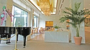 Een lobby met een vleugelpiano, een receptiebalie en een grote kroonluchter.
