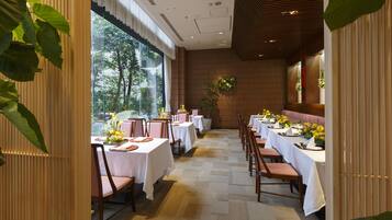 A restaurant with tables set for dining, large windows, and indoor plants.