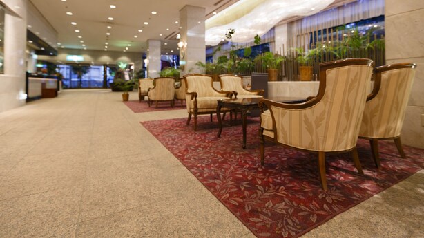 Una hall d'hotel con reception, area salotto con poltrone e un tavolo, e un soffitto decorato.
