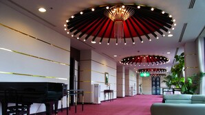 Een hotel lobby met een vleugelpiano, een groene bank en een kroonluchter.