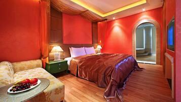 Quarto de hotel com uma cama grande, um sofá, uma mesa de cabeceira e uma cesta de frutas.