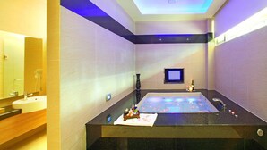 A modern bathroom with a large bathtub, a vanity with a mirror, and a small television. - Le Chateau Hotel (Zhushan)