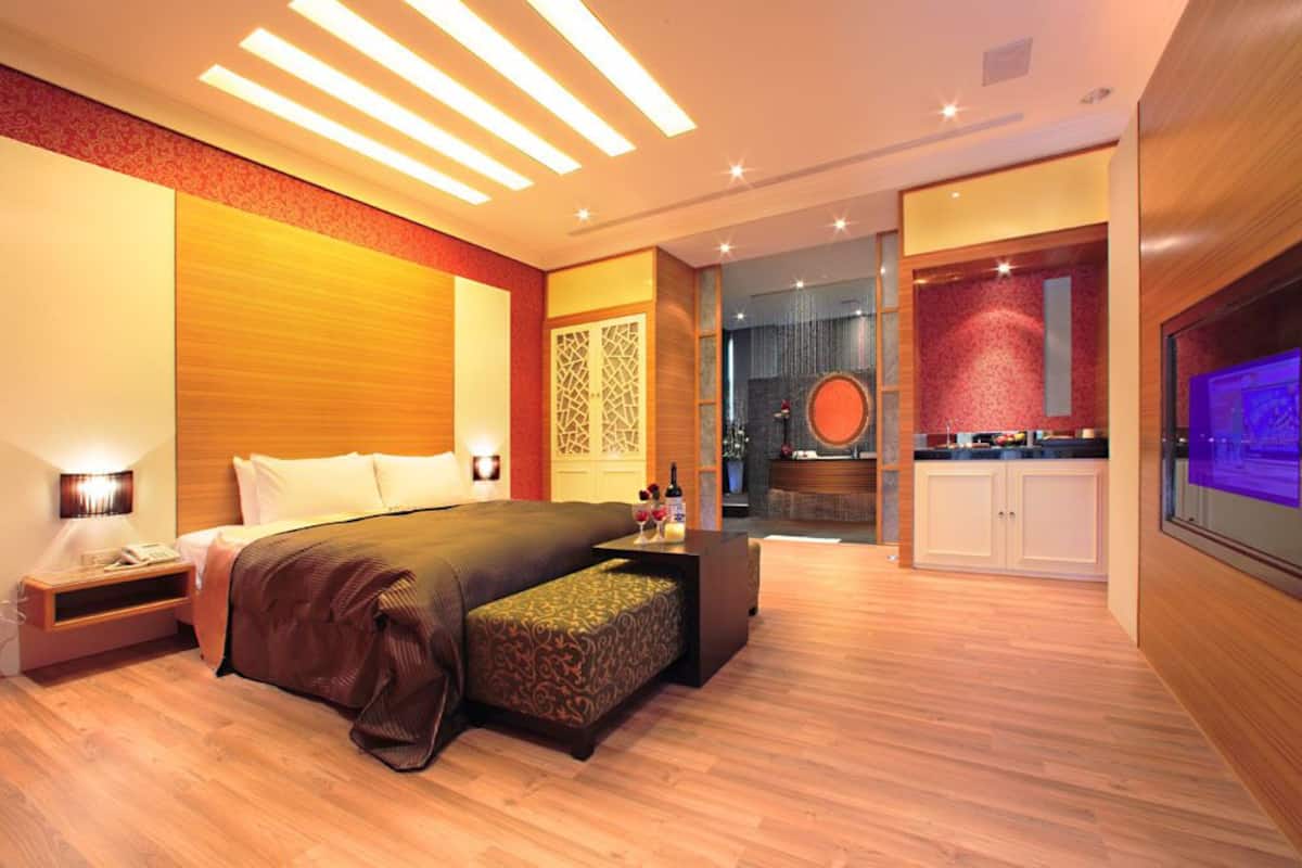 Une chambre d’hôtel moderne dotée d’un grand lit, d’un petit coin salon, d’une kitchenette et d’une télévision.