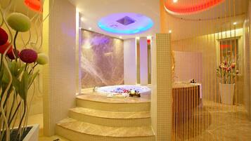 A modern spa area with a hot tub, marble walls, and a decorative plant arrangement.