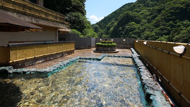 Una piscina exterior cristalina con borde de piedra, rodeada por una valla de madera y un edificio de techo plano.
