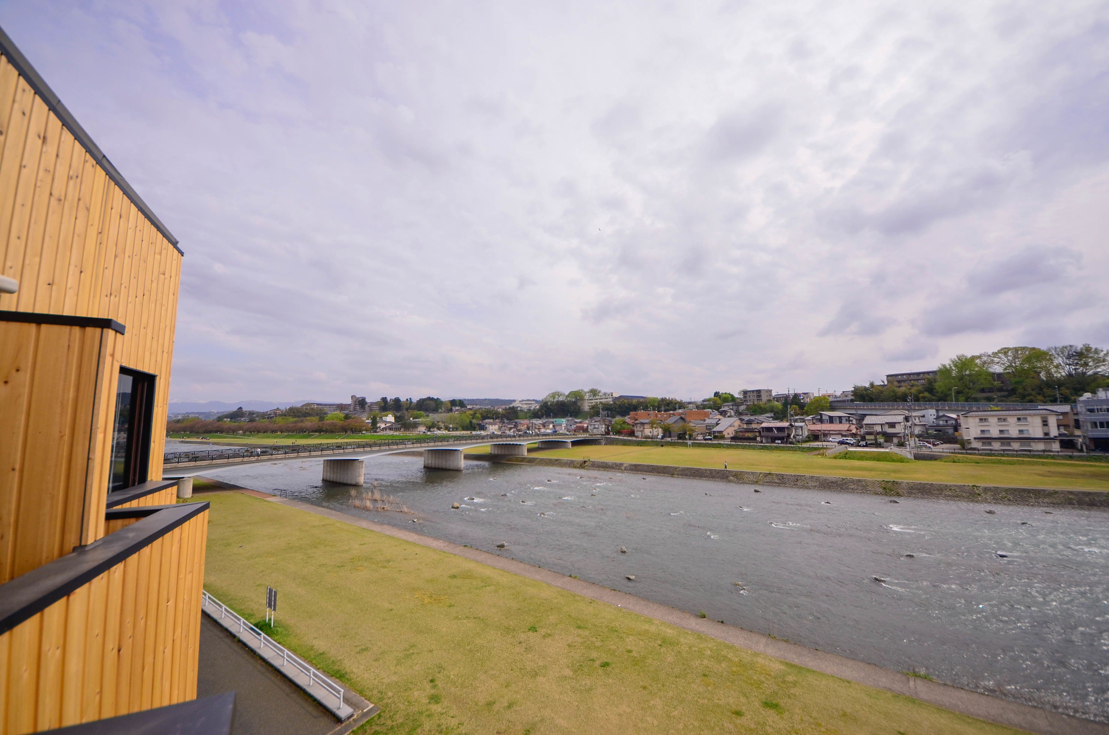 A riverside view with a wooden building, a bridge, and a town in the background.