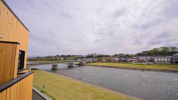 A riverside view with a wooden building, a bridge, and a town in the background.