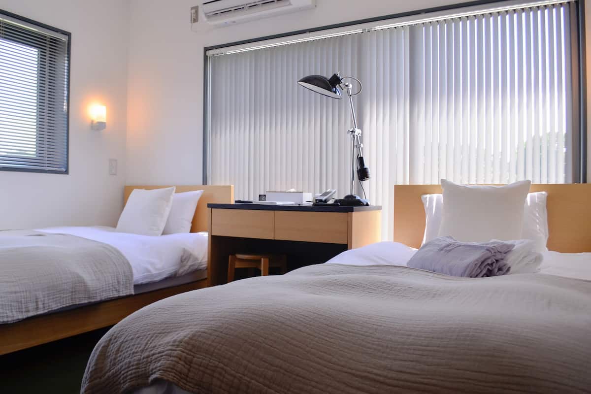 A hotel room with two beds, a desk, and a lamp.