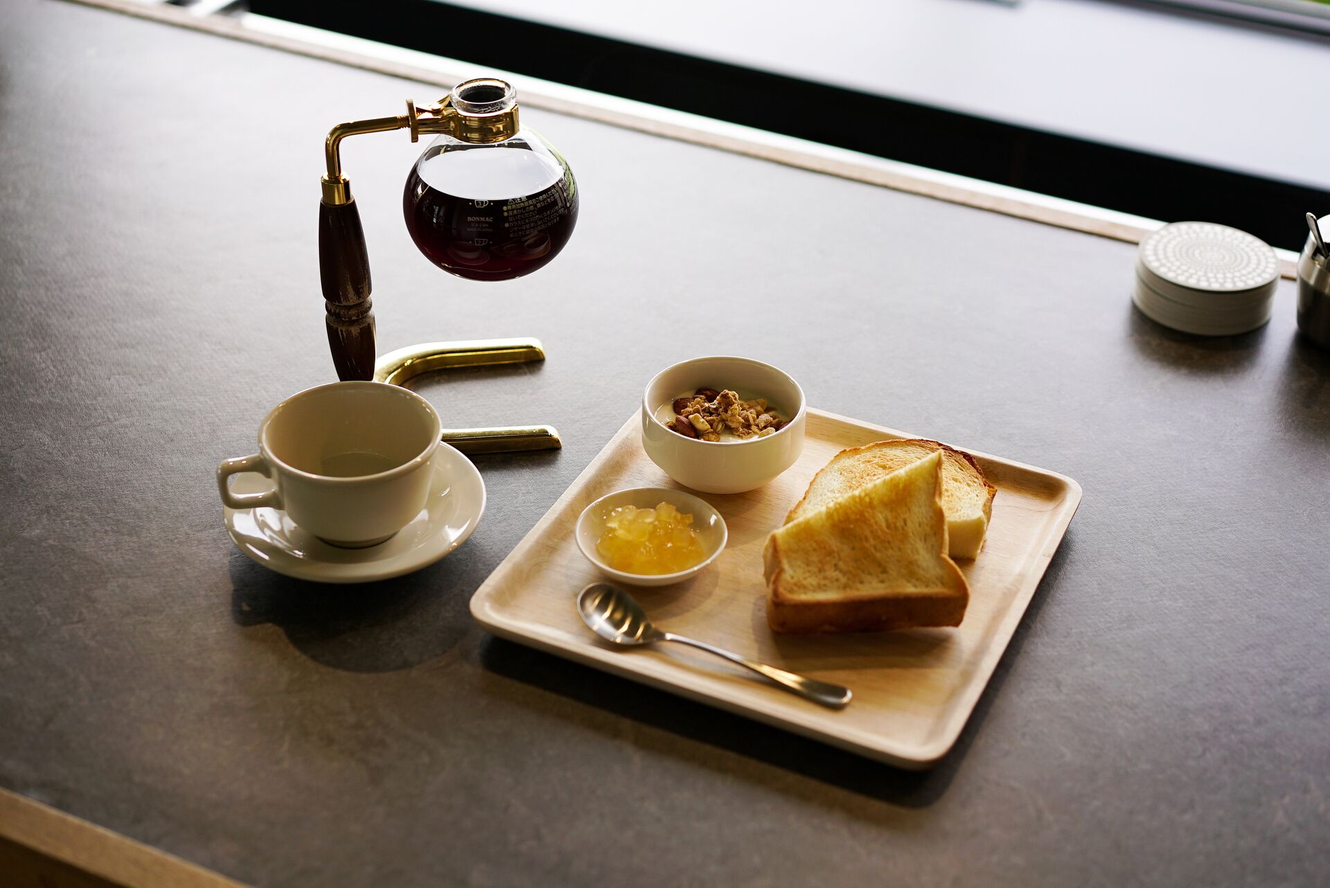 A breakfast tray with toast, a bowl of cereal, a cup, and a small bowl of jam.