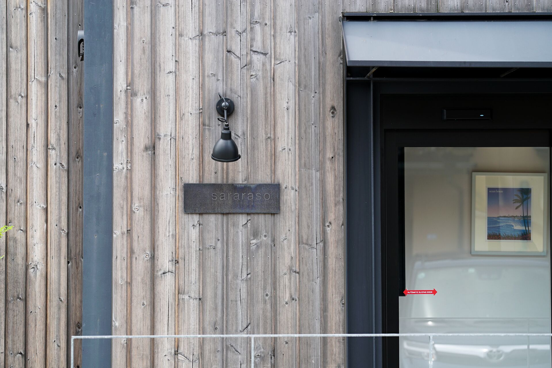 Un mur en bois sur lequel est fixée une plaque en métal portant l’inscription « saraaso », et une porte noire dotée d’un système de coulissement automatique.