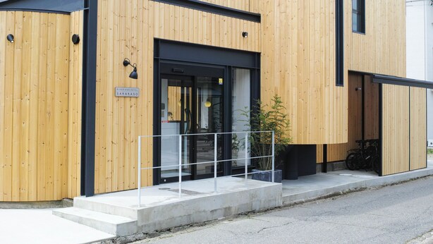 Un bâtiment moderne doté d’une façade en bois, d’une entrée encadrée de noir et d’une enseigne indiquant qu’il s’agit de l’hôtel Riverside Saragos.