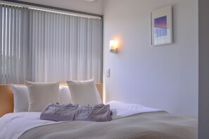 A hotel room with a bed, pillows, a nightstand, a wall-mounted light, and a framed picture. - Sararaso (Kanazawa)