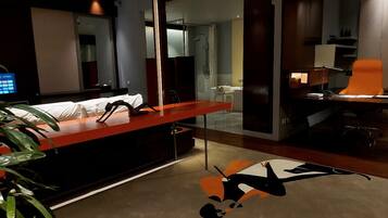 Una habitación de hotel moderna con escritorio, una silla, cama, zona de ducha y un espejo grande.
