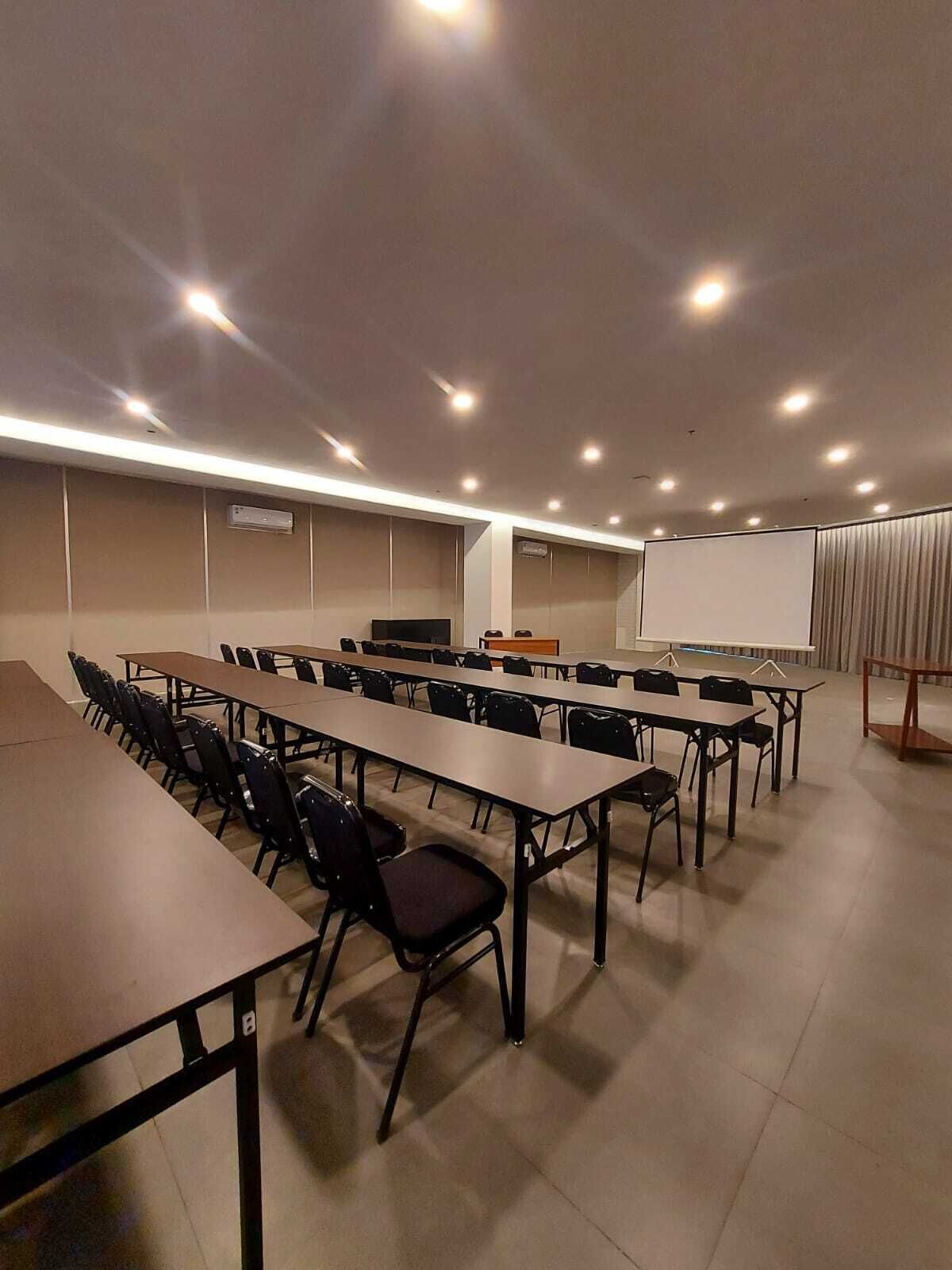 Un salón de conferencias con varias mesas y sillas, una pizarra y una pantalla para proyector.