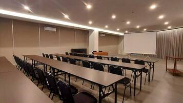 Un salón de conferencias con varias mesas y sillas, una pizarra y una pantalla para proyector.