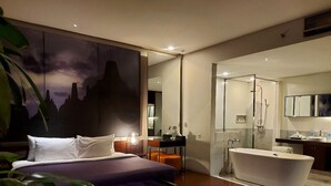 A modern bedroom with a large bed, a walk-in closet, and a separate bathroom with a bathtub and shower. - Kemang Icon Hotel (Jakarta)