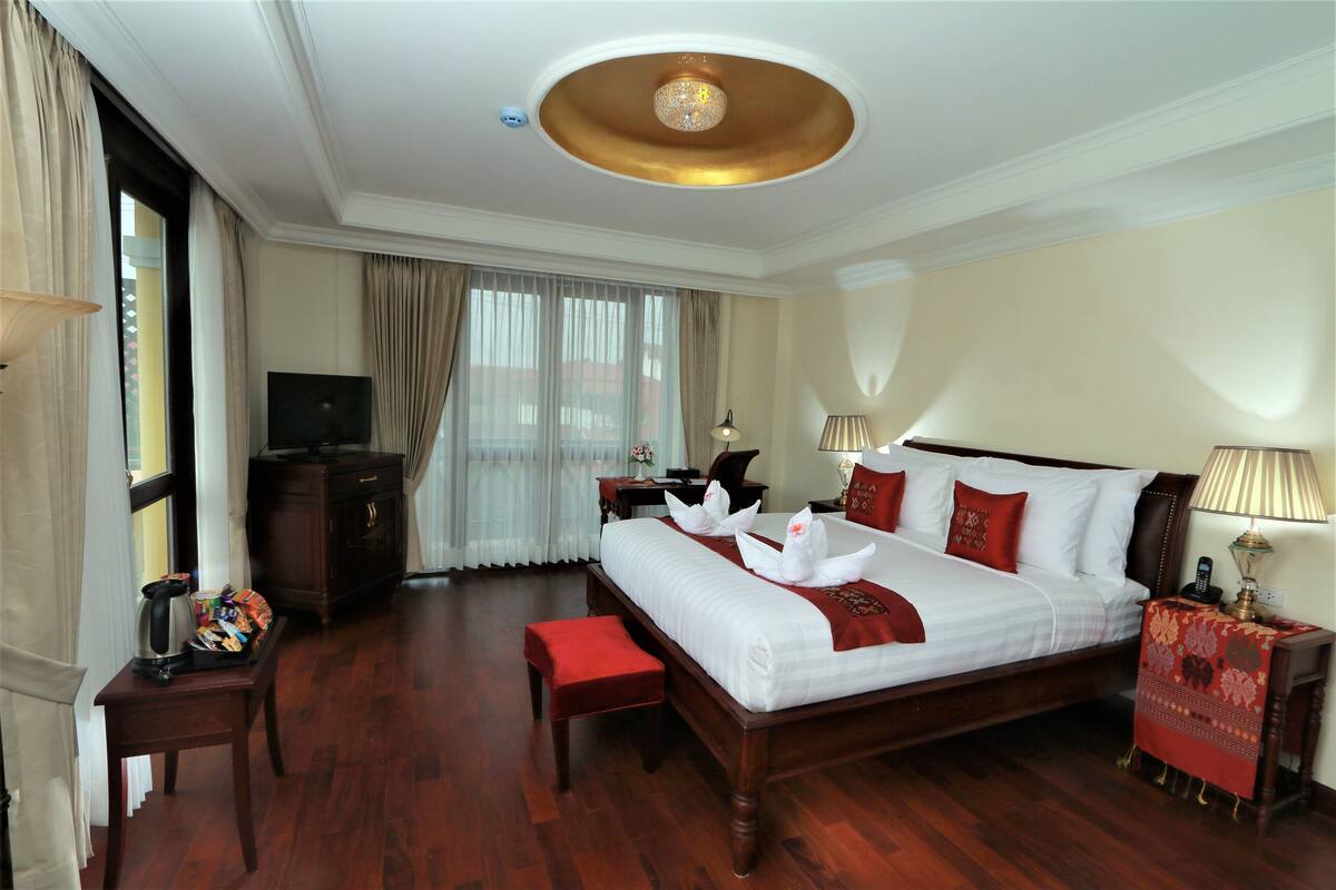 A hotel room with a large bed, a television, a desk, and a window with curtains.