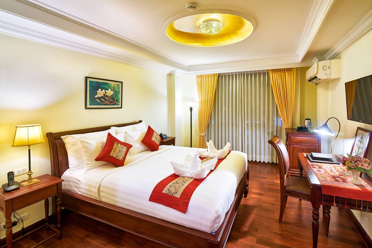 A hotel room with a neatly made bed, a desk with a lamp, a chair, and a television on the wall.