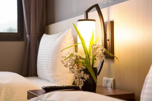 A hotel room with a bed, a bedside table with a remote control, a lamp, and a potted plant with white flowers. - Yun Shue Tang (Ji'an)
