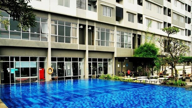 A swimming pool adjacent to a multi-story building with large windows and balconies. - High Livin Apartment Baros (Cimahi)